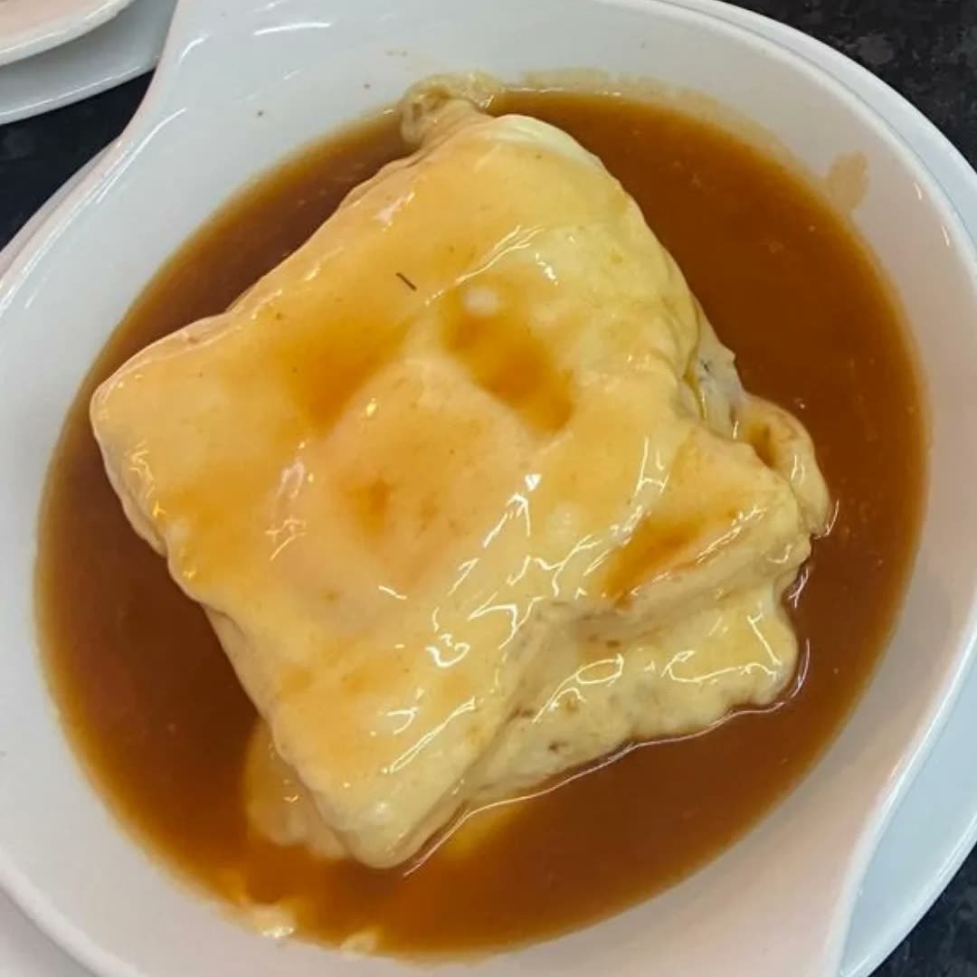 Francesinha com ovo servida em travessa funda, coberta de molho